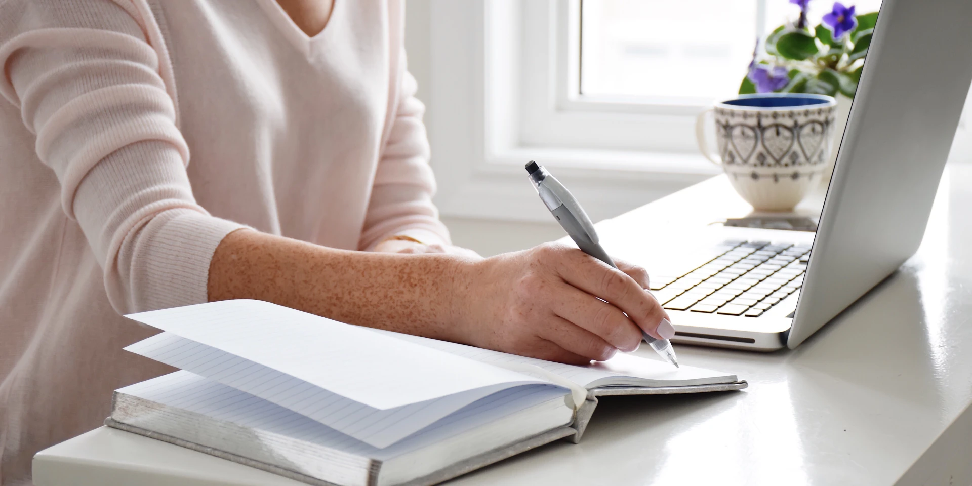 Woman Setting at a Desk taking notes from hey labtop